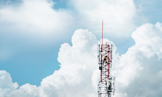 A 5G transmission tower in front of a blue sky and large white clouds