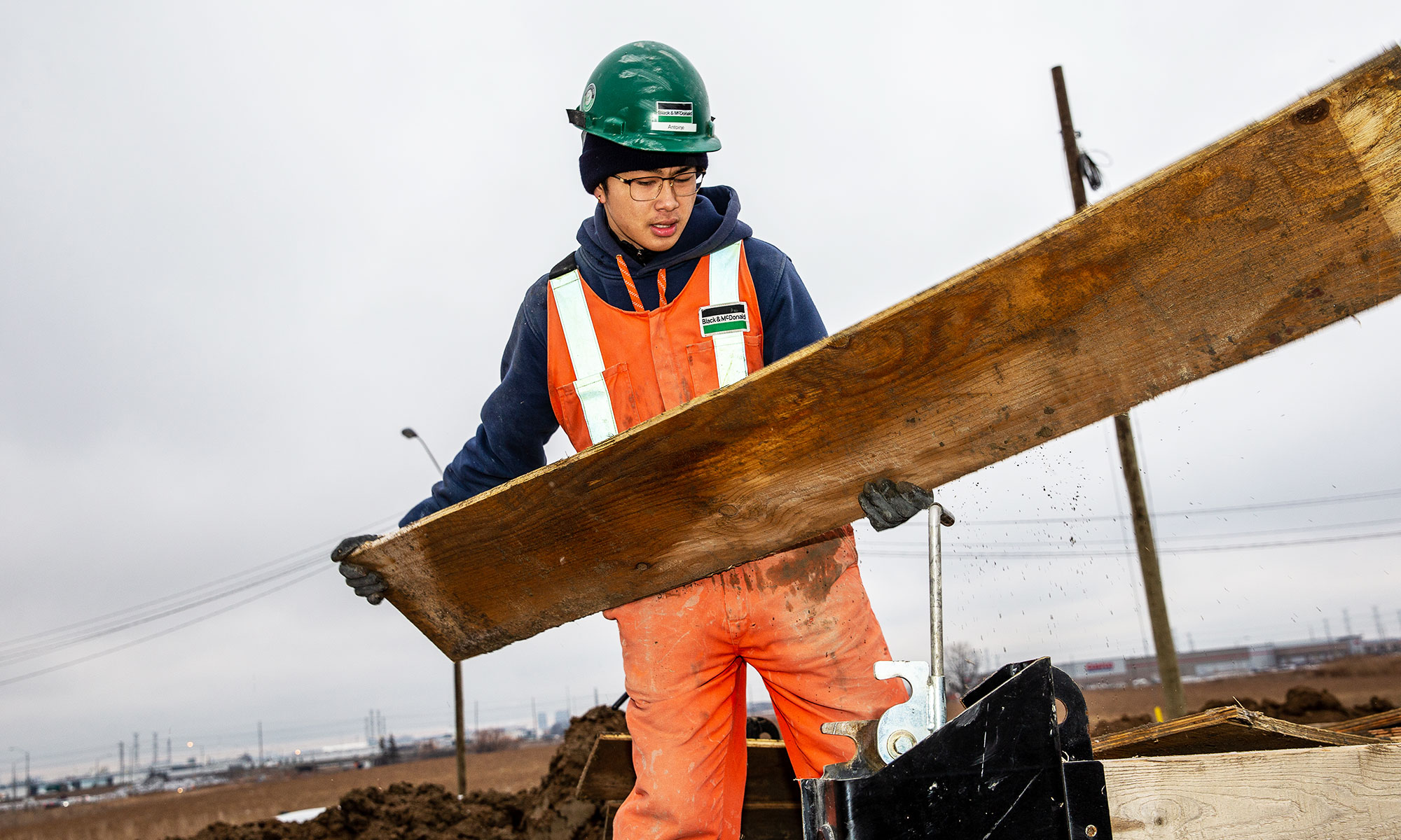 A Black & McDonald field worker moving lumber at a construction site