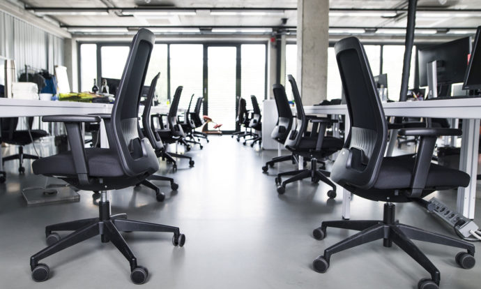 Une salle de bureaux vide, remplie uniquement de chaises, de bureaux et d’ordinateurs.