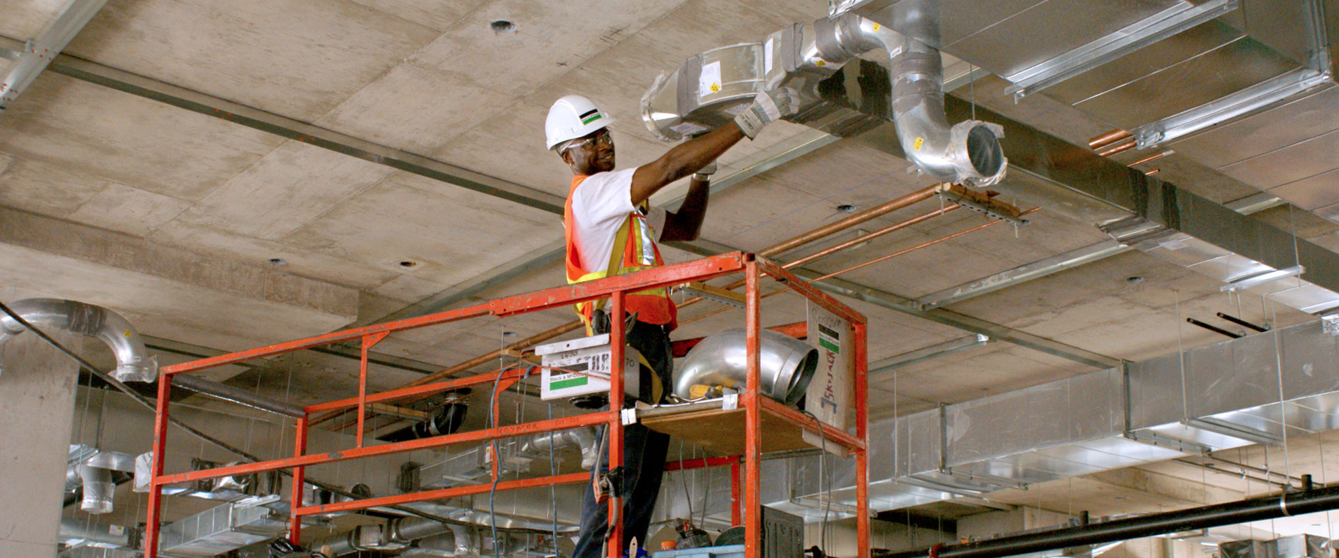 B&M tradesperson on an elevated platform installing sheet metal for a ducting project